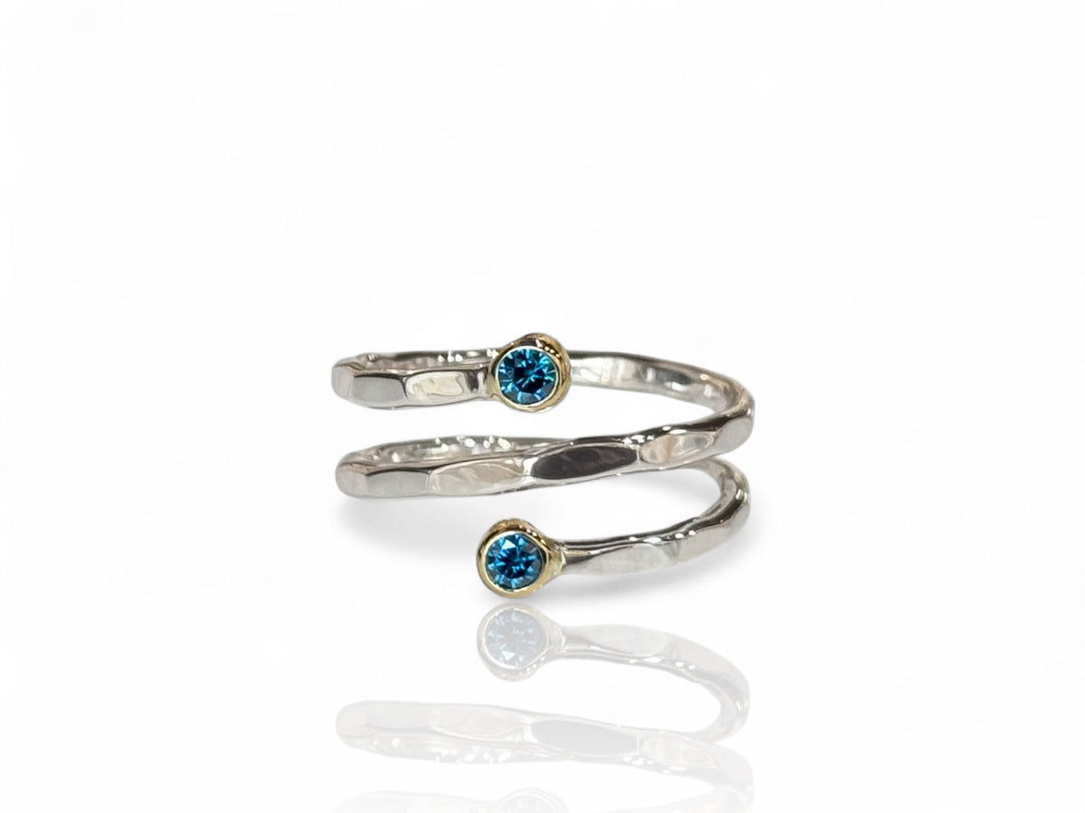 Minimalist spiral ring with blue diamonds in yellow gold bezels on a facet-textured silver band