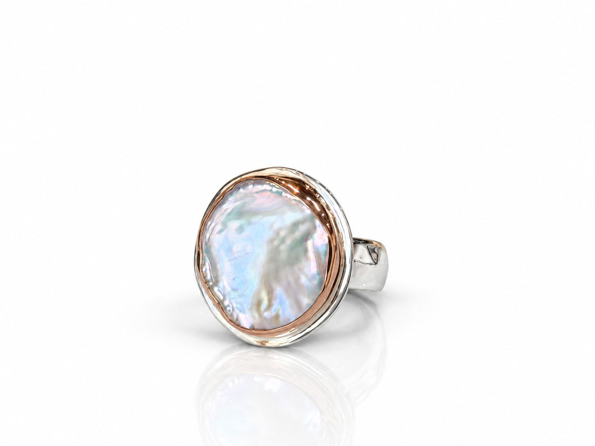 Organically shaped freshwater pearl with a cream and rosy luster in a bezel on a silver and rose gold ring