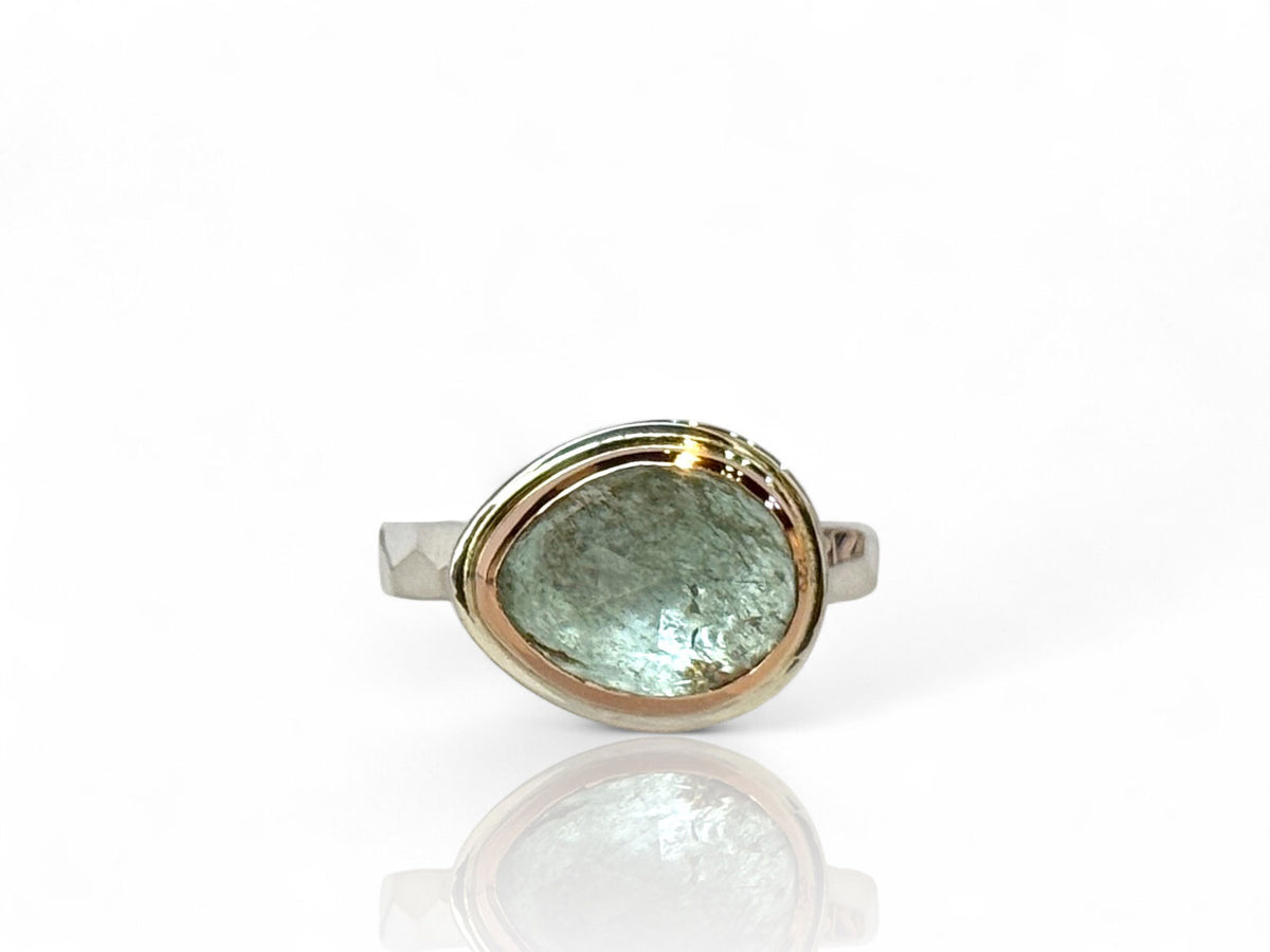 Icy blue rose-cut aquamarine freeform stone in a 14kt rose gold bezel on a faceted-texture silver band