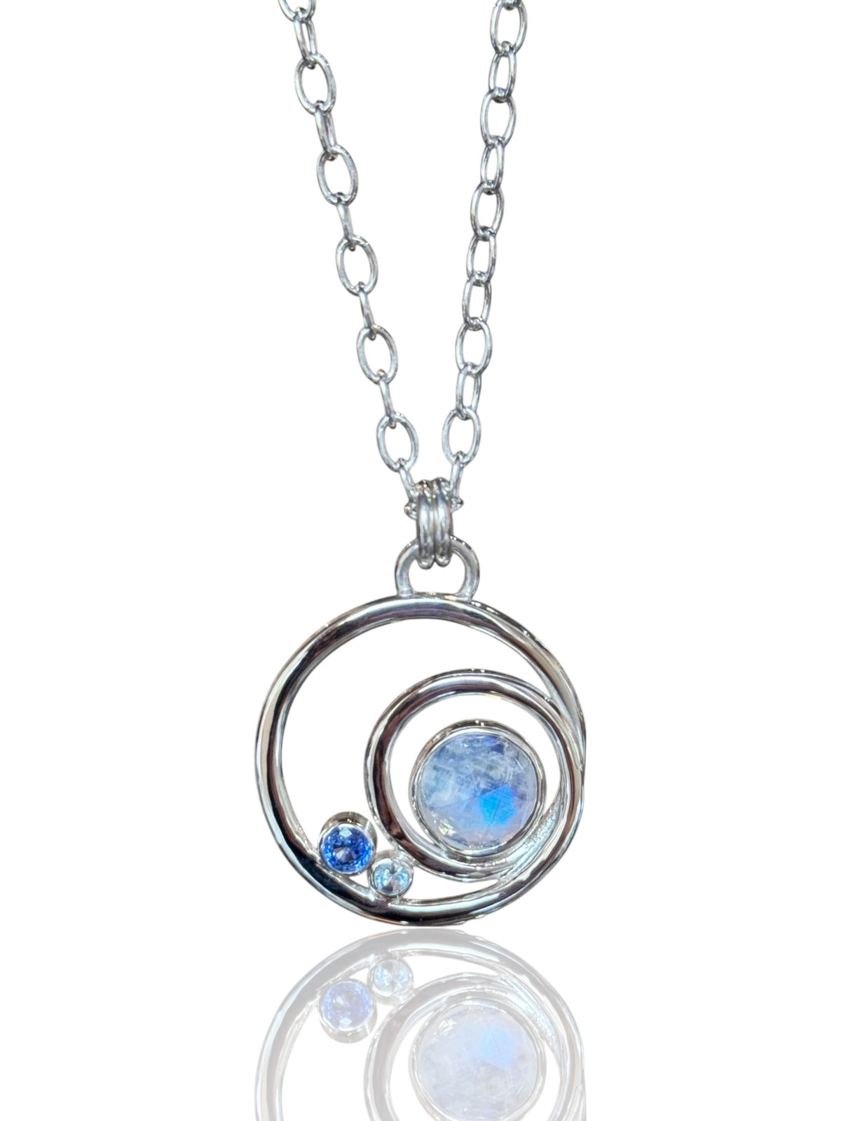 Round moonstone in a sleek silver orbital pendant with cornflower blue sapphire and sky blue topaz accents