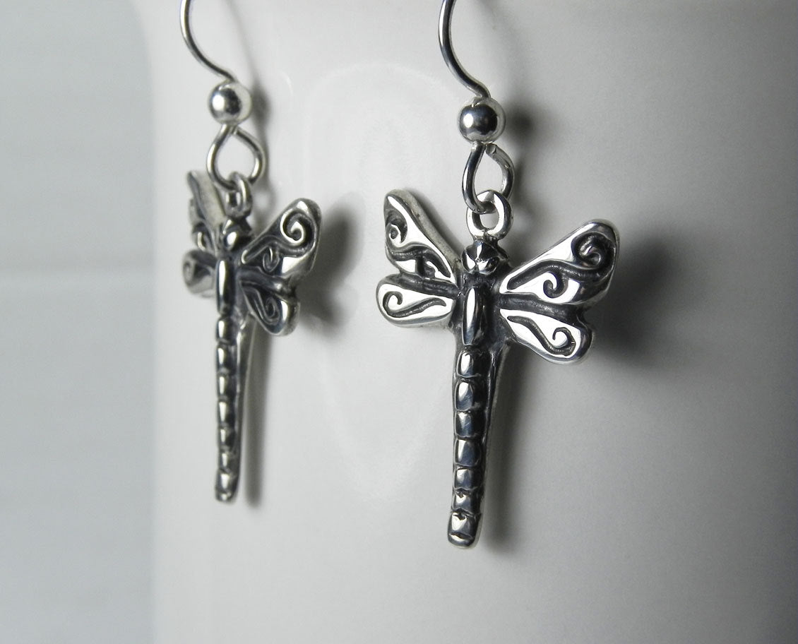 Close view of a sterling silver dragonfly earring showing its dark oxidized swirl details