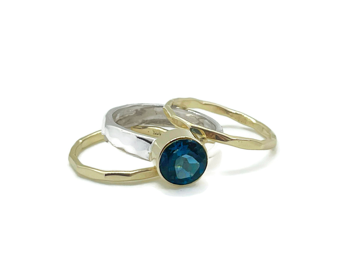 8mm deep blue London blue topaz in a yellow gold bezel on a hammered sterling silver stack ring set