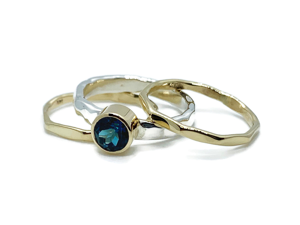Deep greenish-blue London blue topaz in a 14kt yellow gold bezel on a hammered sterling silver stack ring set