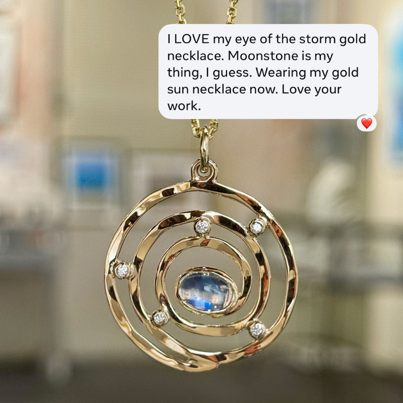 A gold-toned spiral pendant necklace with a round blue moonstone center and small clear stones, shown against a blurred indoor background with a text bubble overlay describing the necklace.